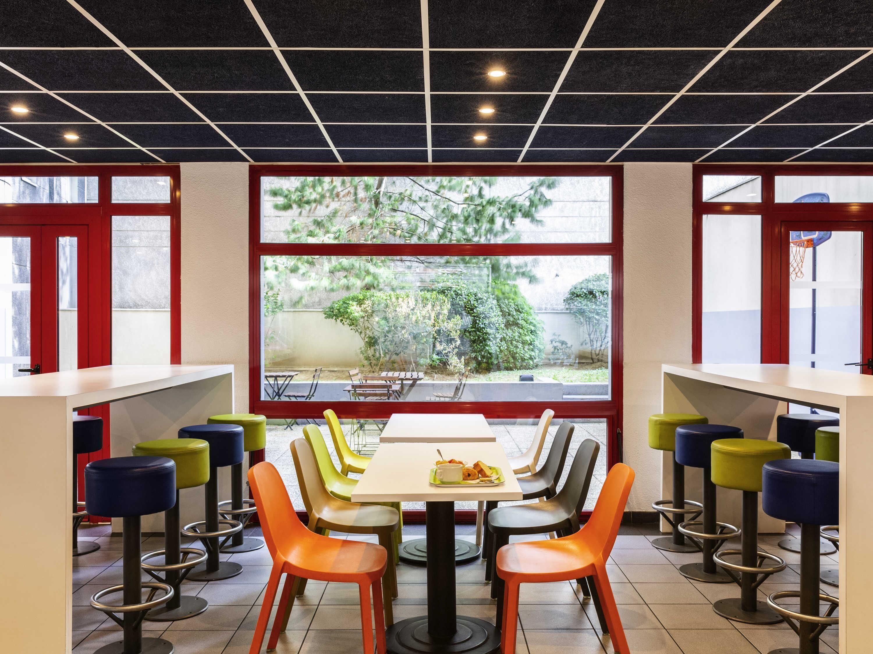 A dining area with a large window, multiple tables, and colorful chairs.
