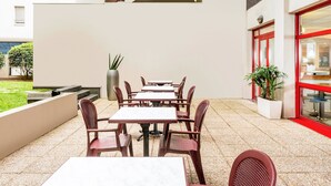 An outdoor patio area with tables and chairs, a staircase, and a building with a red-framed window. - ibis budget Paris Porte d'Italie Est (Le Kremlin-Bicetre)