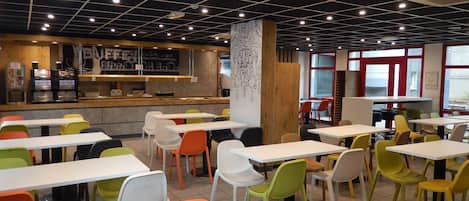 Un café moderno con varias mesas y sillas, una barra con un panel de menú y un adorno en la pared.