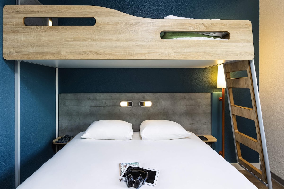 Un lit superposé avec une tête de lit en bois, une table de chevet avec une lampe et un oreiller sur le lit du bas.