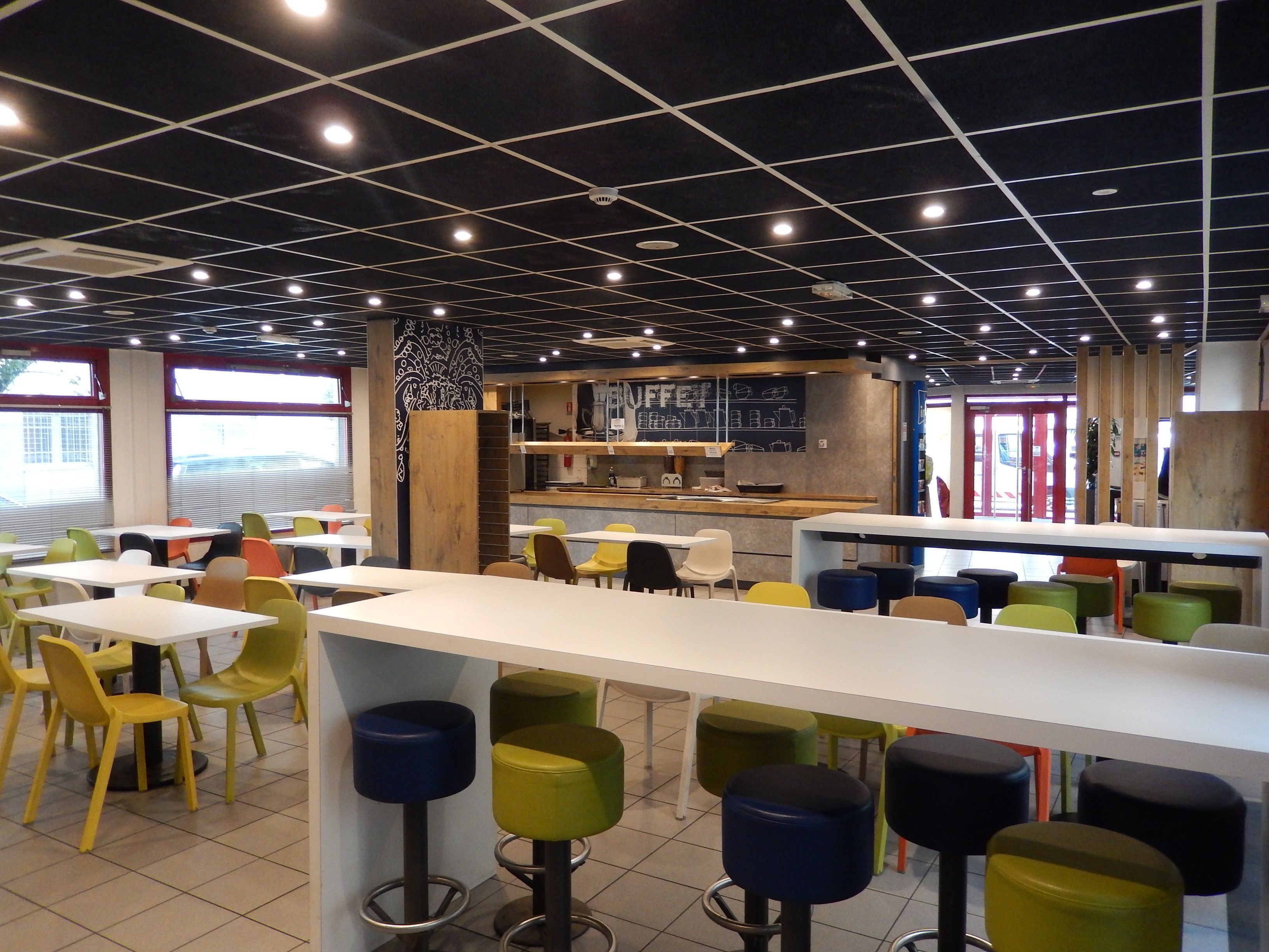A modern cafe interior with high ceilings, grid-patterned ceiling lights, and a central bar area.
