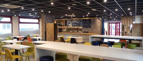 A modern cafe interior with high ceilings, grid-patterned ceiling lights, and a central bar area.