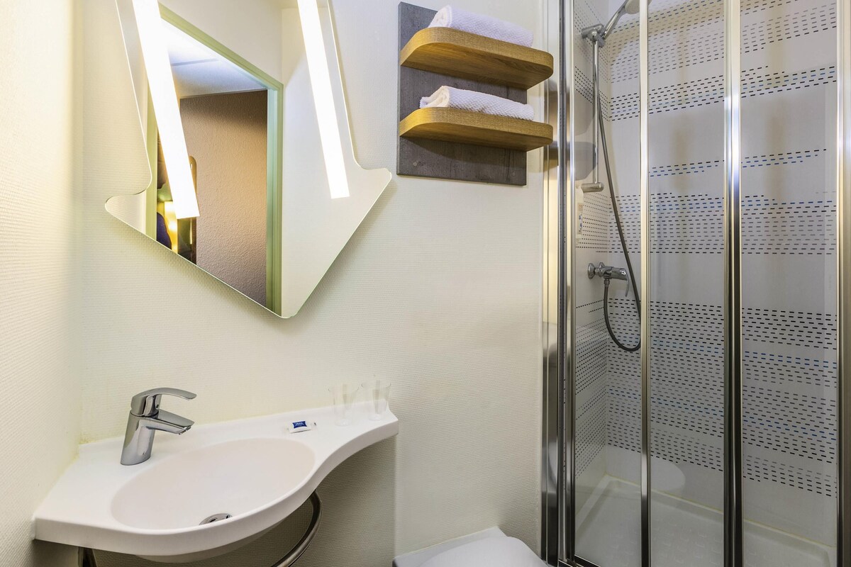 A bathroom with a white sink, a mirror, a shower with a glass door, and a towel rack.