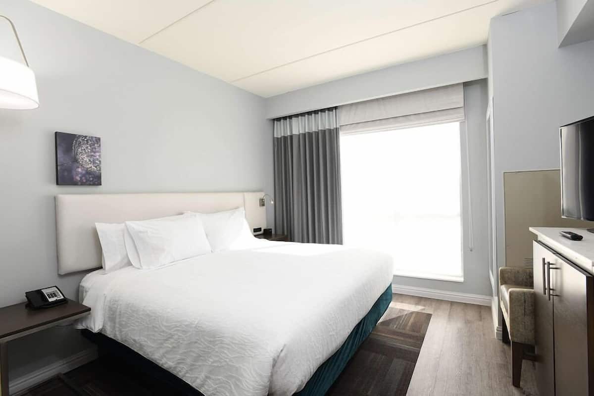 A hotel room with a large bed, a desk with a TV, and a window with curtains.