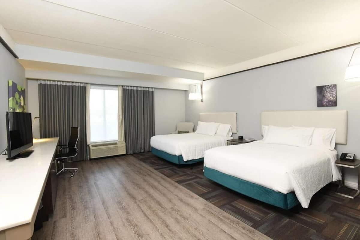 A hotel room with two beds, a desk, a TV, and a window with curtains.