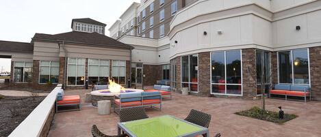 A hotel courtyard with outdoor seating, a fire pit, and a large glass facade.