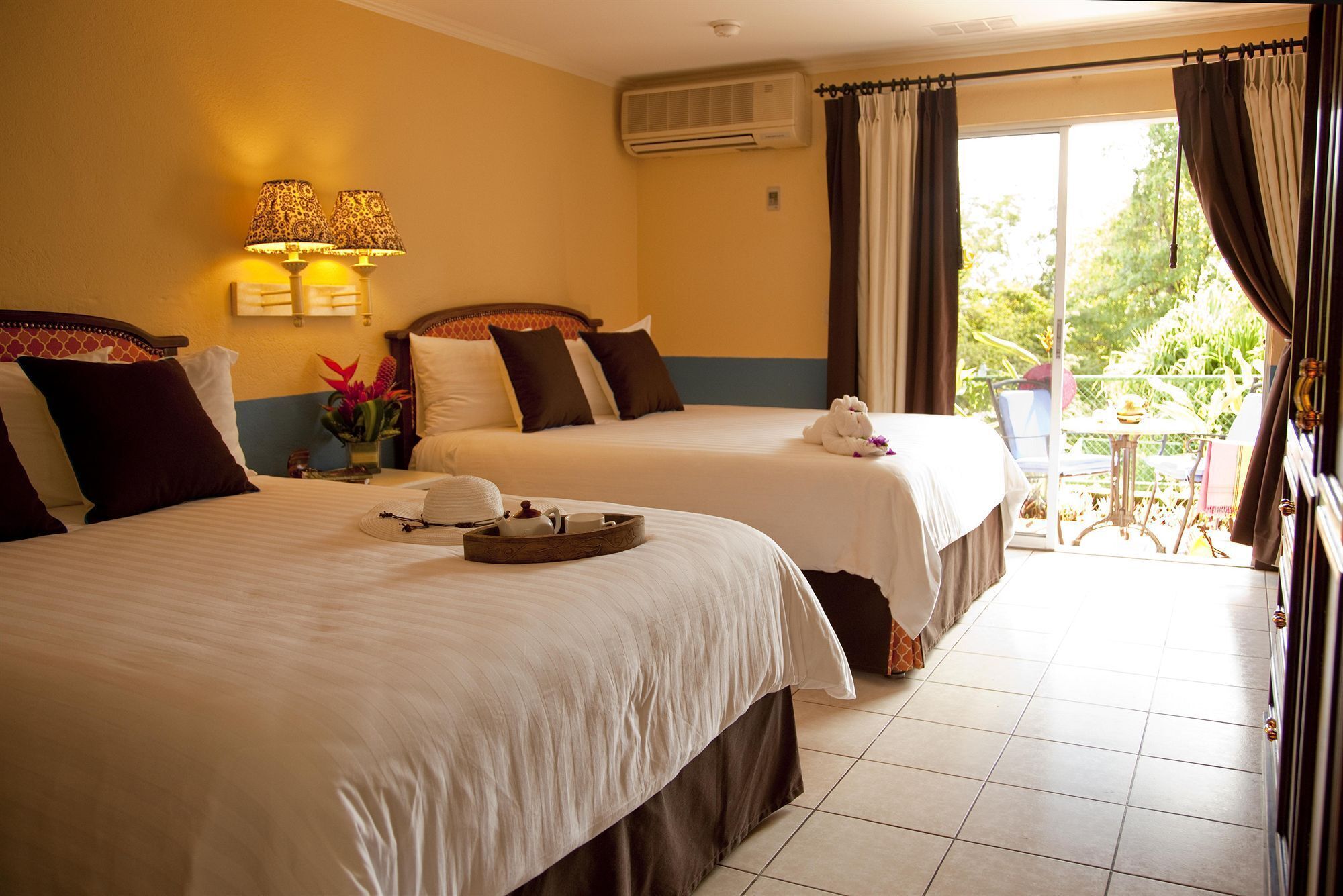 A hotel room with two beds, a balcony with a table and chairs, and an air conditioning unit on the wall.