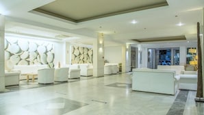 A spacious lobby with a modern design, featuring a central seating area with sofas and armchairs, a patterned wall, and a clean, tiled floor. - Semiramis Village (Hersonissos)