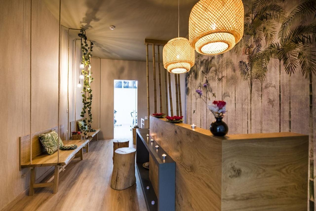 Un mostrador de recepción de madera con un jarrón de flores, lámparas de ratán colgantes y un banco con cojín.