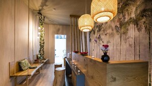 A wooden reception desk with a vase of flowers, hanging rattan lamps, and a bench with a cushion. - Semiramis Village (Hersonissos)