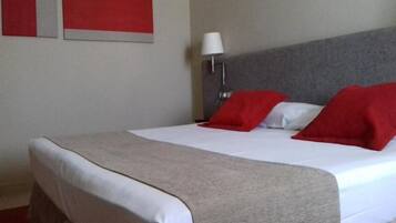 A hotel room with a bed, a headboard, a bedside lamp, and two red pillows.