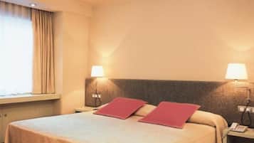 Habitación de hotel con cama, dos lámparas de noche, una ventana con cortinas y una mesita de noche con teléfono.