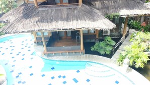 Zona de piscina con una estructura de techo de paja, una terraza de madera y una pequeña piscina con borde de azulejos.
