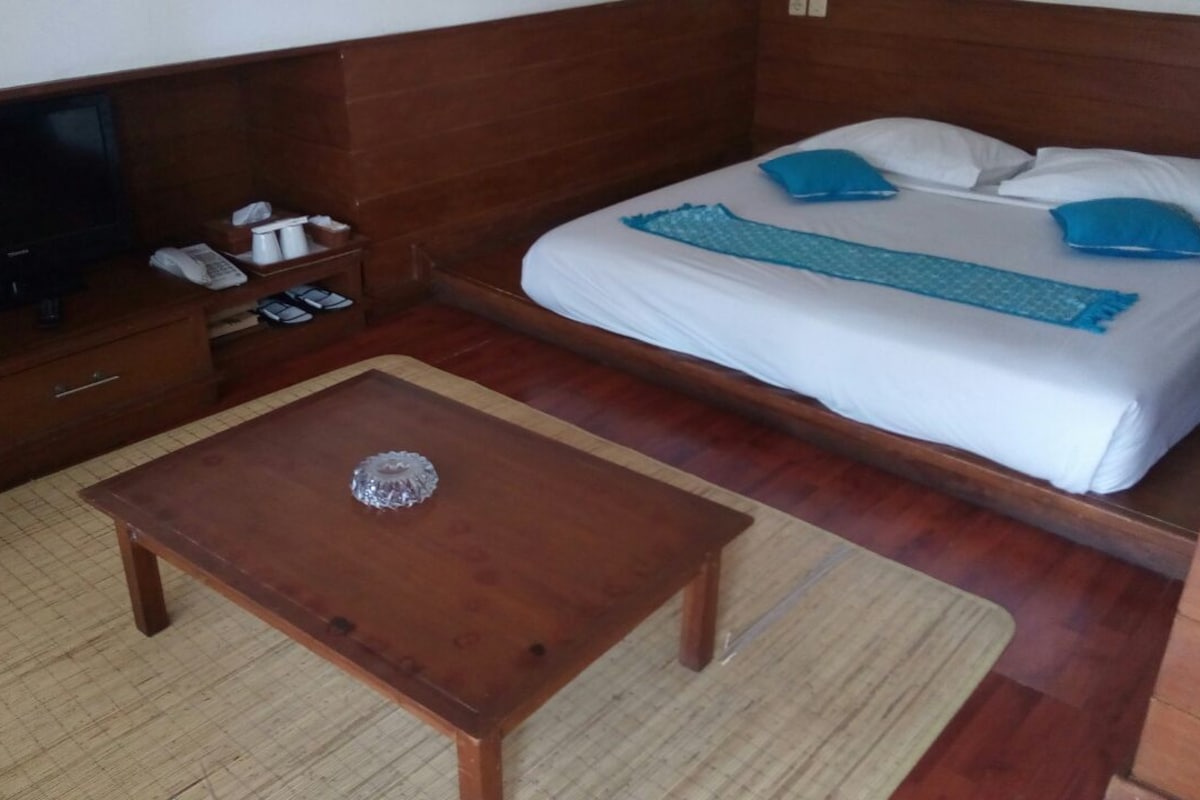 A hotel room with a bed, a wooden nightstand with a television, a small table with a decorative item, and a carpeted floor.