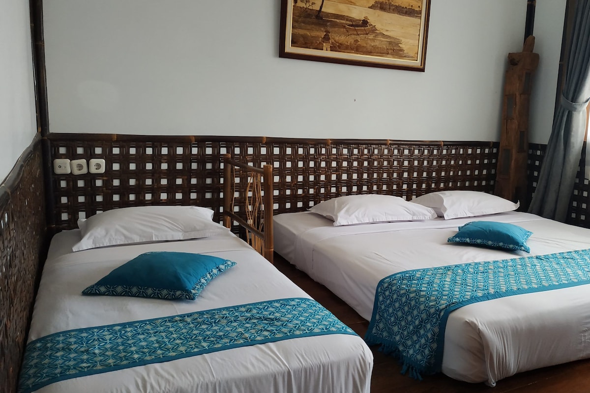 Two single beds with white linens and blue decorative pillows, a wooden headboard with a lattice design, and a painting on the wall.