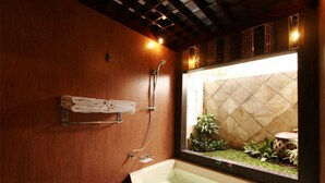 Un baño con pared de madera, bañera integrada, ducha y un espejo grande que refleja vistas de un jardín.