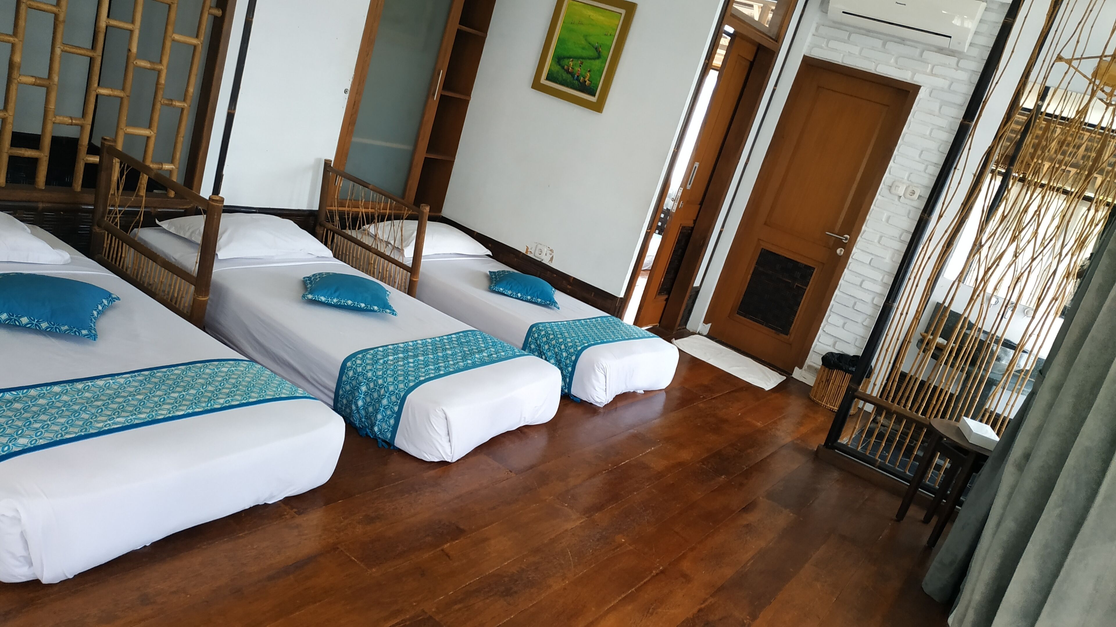 A hotel room with three single beds, a wooden chair, a bamboo screen, and a white brick wall.