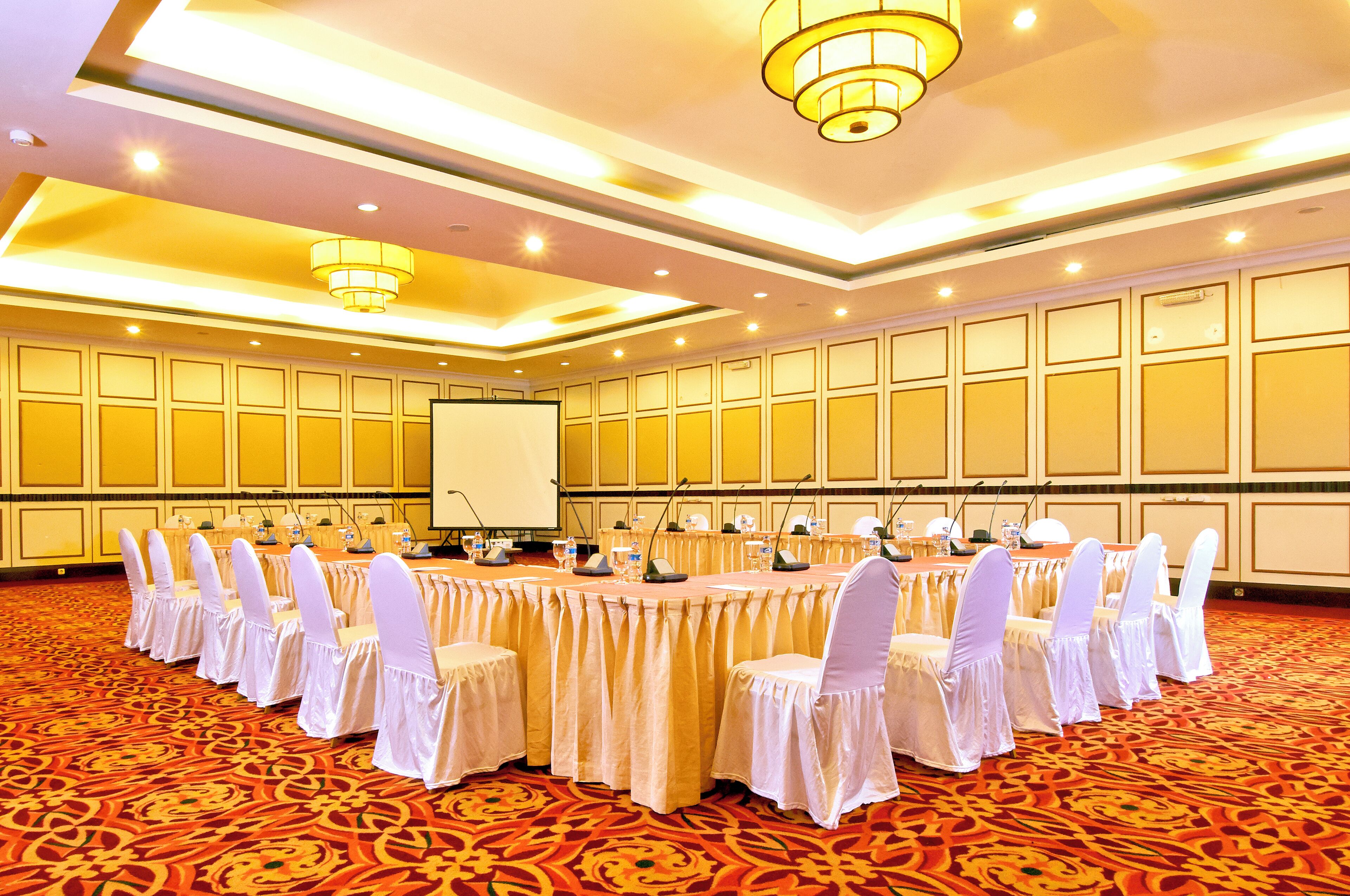 A conference room with a long table, white chairs, and a projector screen.