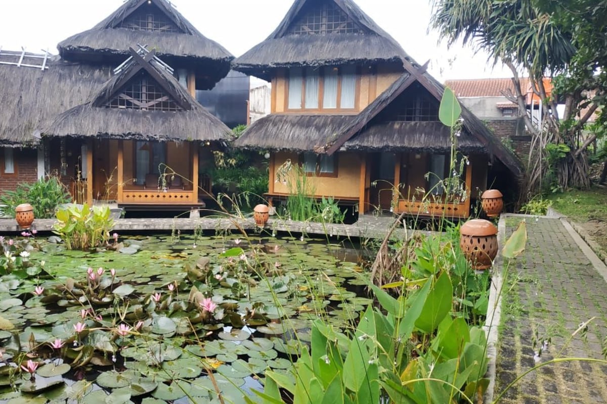 Traditional thatched-roof houses with a pond and lotus flowers.
