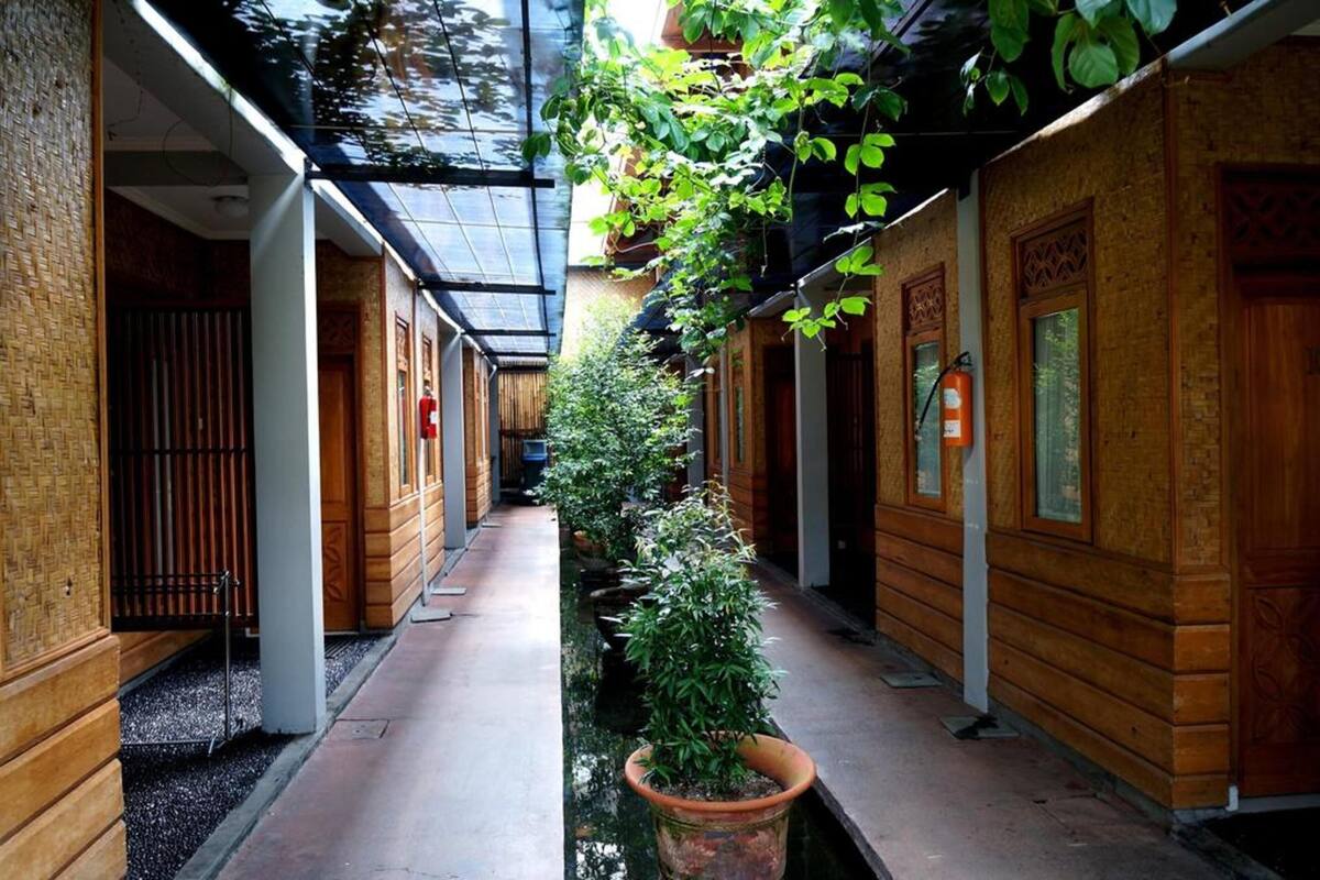 Passadís estret amb parets de fusta, una font al centre i plantes penjants.