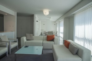 Una sala moderna con un sofá, sillones, una mesa de centro y un comedor al fondo.