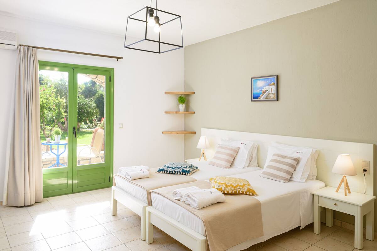 A hotel room with a large bed, bedside tables, a green door, and a view of the outdoors.