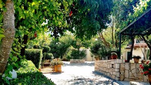 A paved pathway lined with lush greenery and potted plants, leading to a stone wall and a building with a tiled roof. - Villa Vicky (Hersonissos)