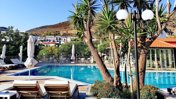 A pool area with lounge chairs, umbrellas, and a view of a hillside town. - Villa Vicky (Hersonissos)