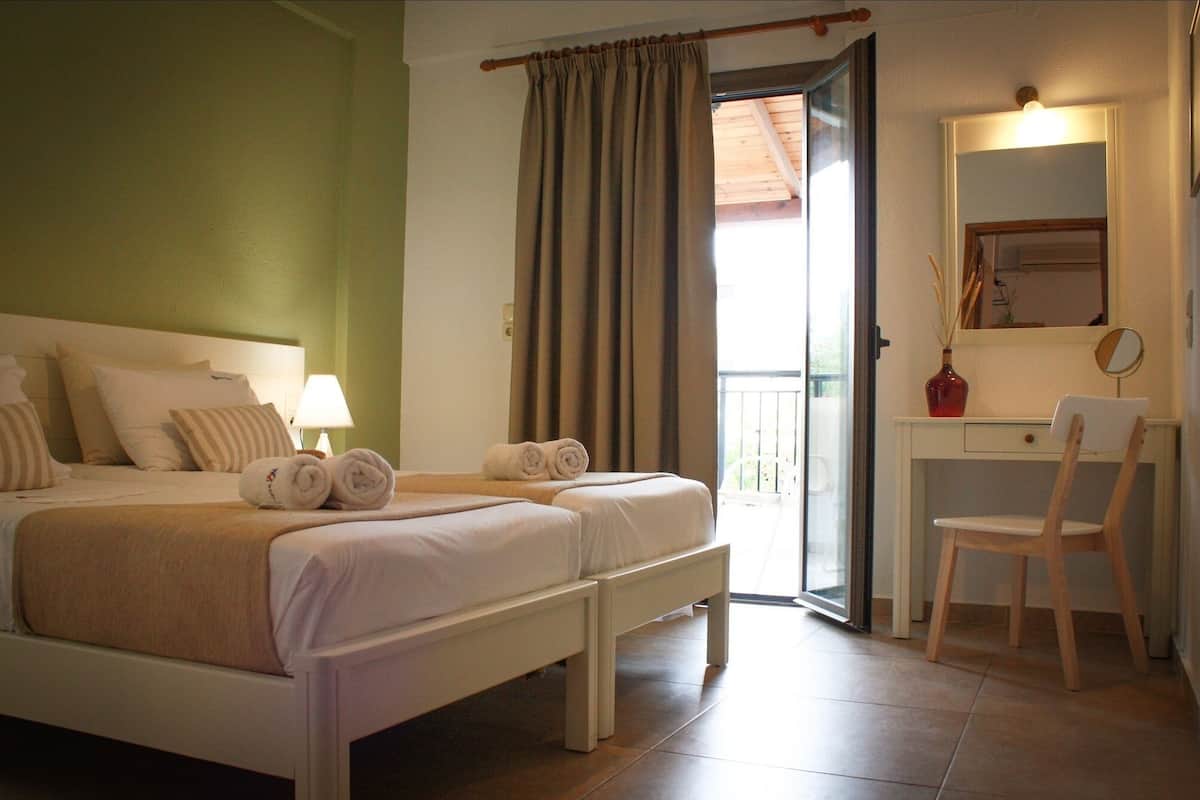 A hotel room with a bed, a desk, a chair, a mirror, and a window with curtains.