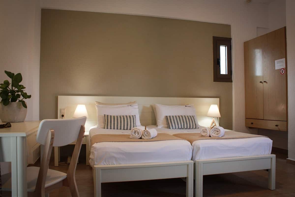 A hotel room with two beds, a desk, chairs, a potted plant, and a wardrobe.