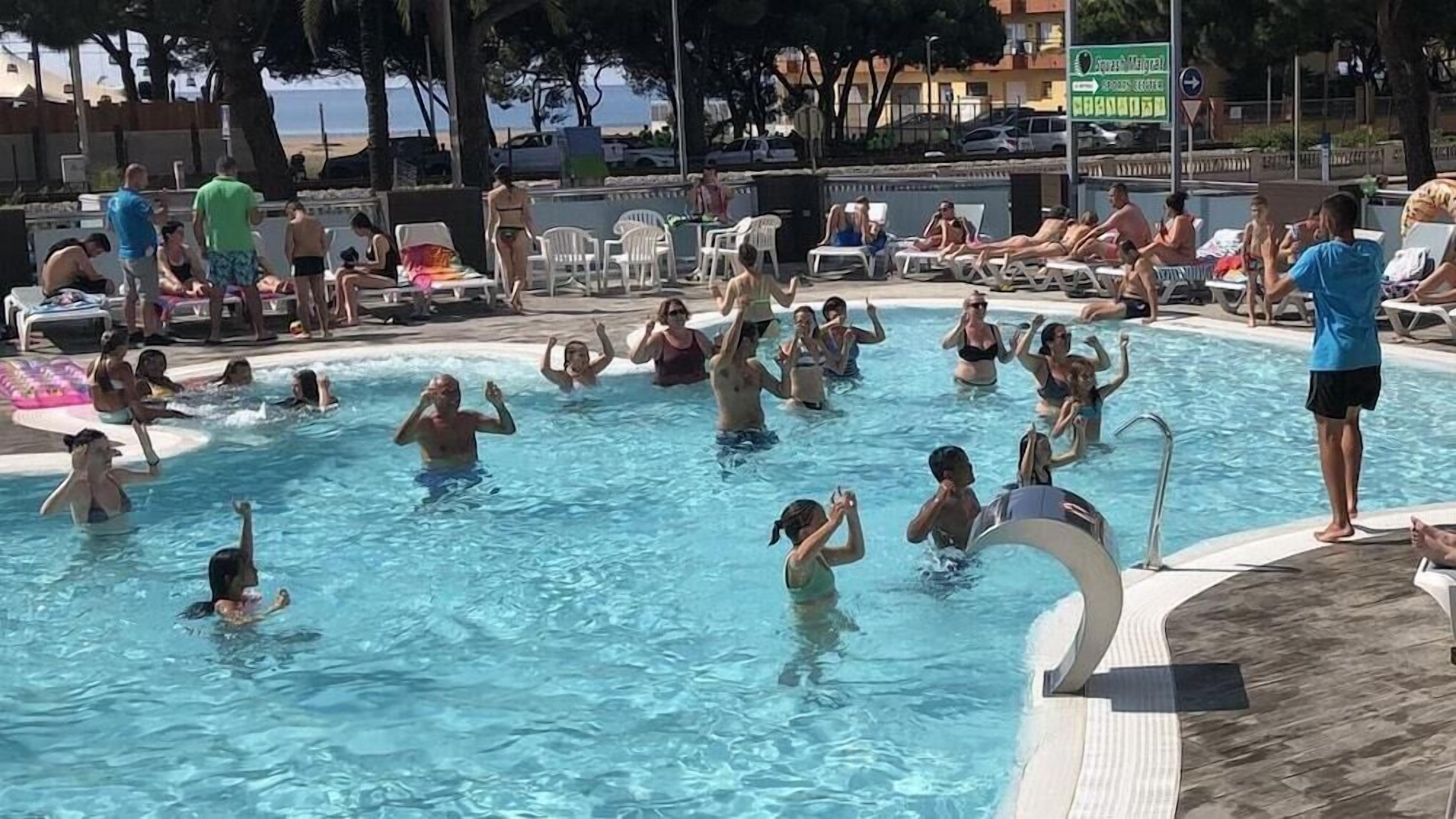 A public swimming pool with people swimming and sunbathing.