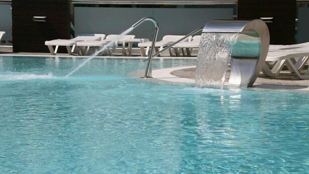 A swimming pool with a water feature, lounge chairs, and a modern architectural design. - Reymar Playa (Malgrat de Mar)