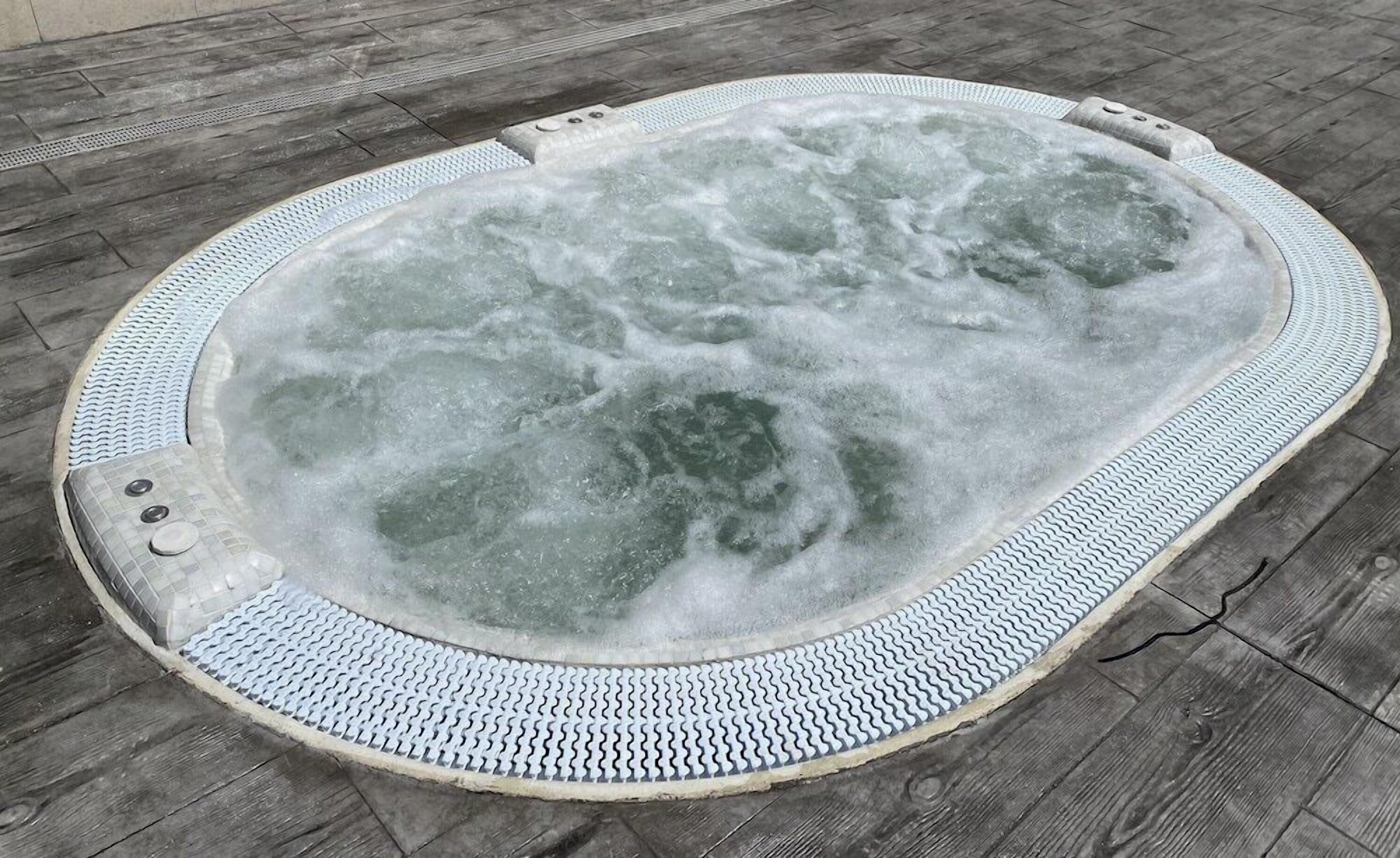 A hot tub with a textured edge and a tiled floor surrounding it.