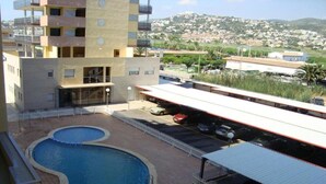 A building with a swimming pool, a covered parking area, and a view of a hilly town. - Pompeya (Peniscola)