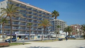 A multi-story hotel with balconies, palm trees, and a paved area with benches. - Pompeya (Peniscola)