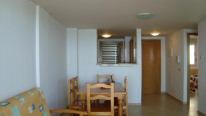 A living room with a wooden dining table and chairs, a sofa, and a window with blinds. - Pompeya (Peniscola)