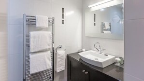 Une salle de bain moderne avec une douche à l’italienne en verre, un lavabo blanc et un meuble-lavabo aux tons foncés.