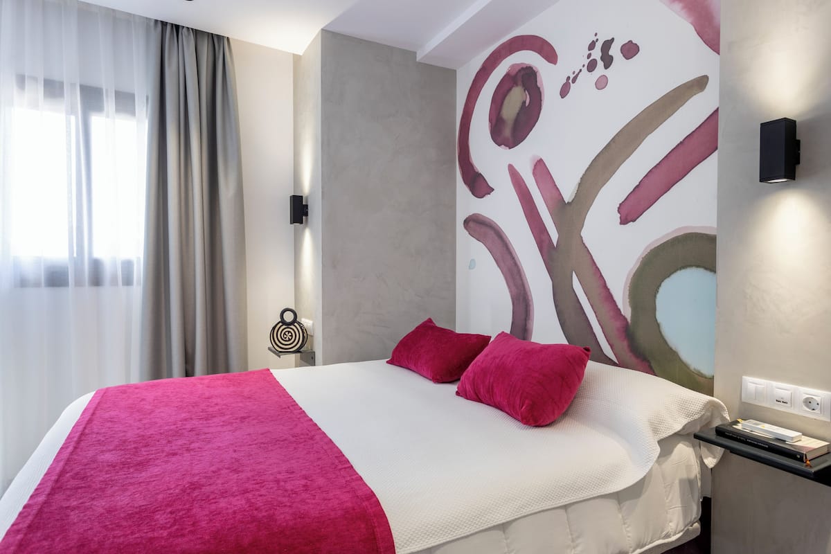 A modern hotel room with a large bed, a bedside table, and a wall with abstract art.