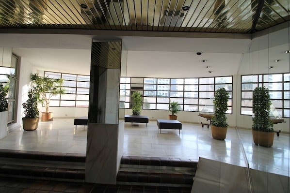 Un hall d’entrée spacieux, doté de grandes fenêtres, de plantes en pot et d’un escalier moderne.
