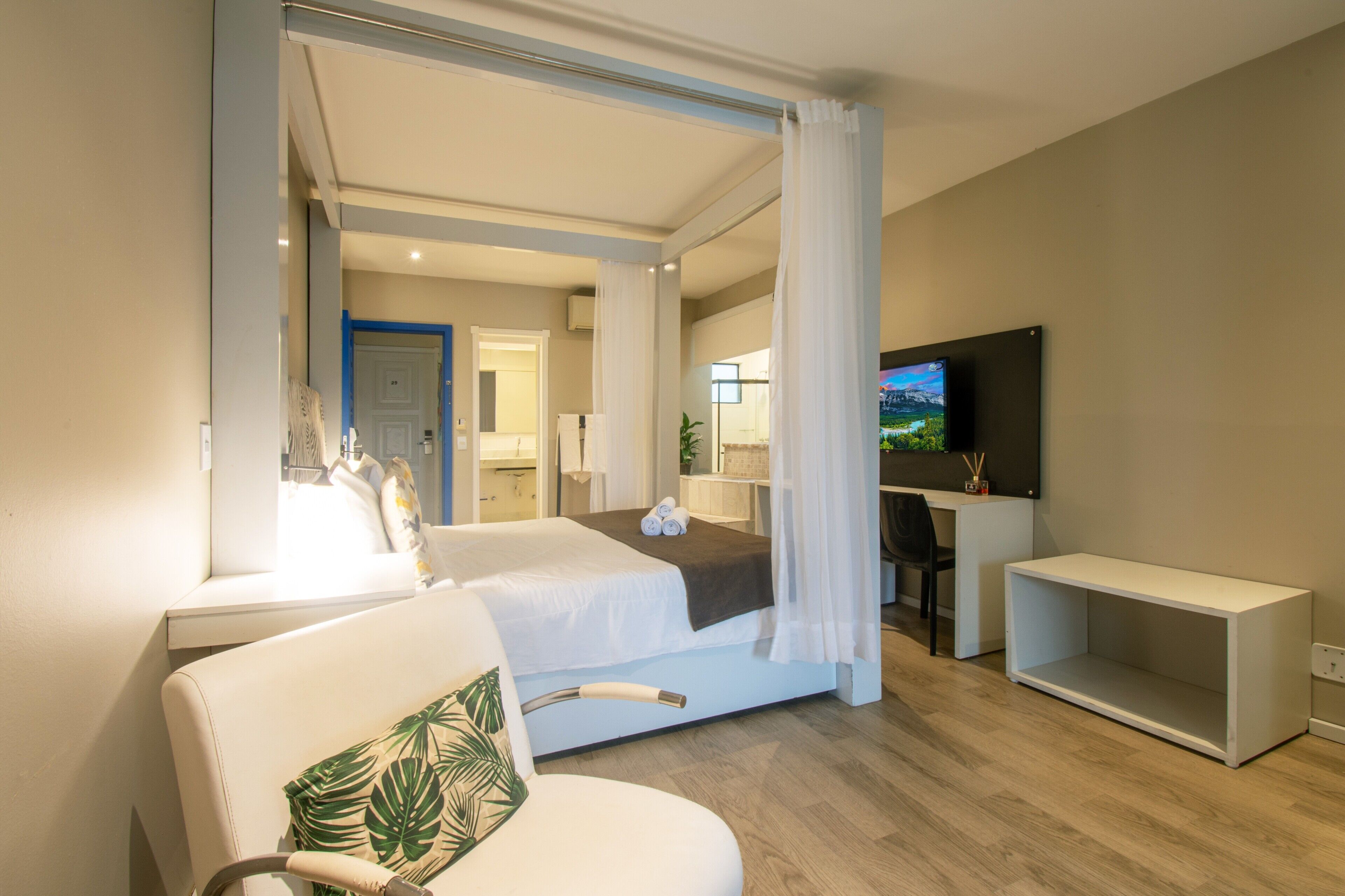 Una habitación de hotel moderna con una cama grande, televisor, escritorio y zona de ducha.