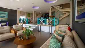 A modern living room with a sofa set, a coffee table, and a staircase with teal railings. - Pousada Aroma do Mar (Búzios)