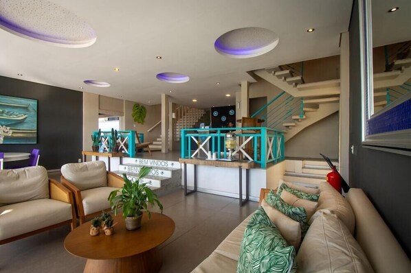 A modern living room with a sofa set, a coffee table, and a staircase with teal railings. - Pousada Aroma do Mar (Búzios)