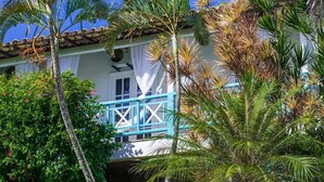 A building with a white facade, a blue balcony, and lush tropical vegetation. - Pousada Aroma do Mar (Búzios)
