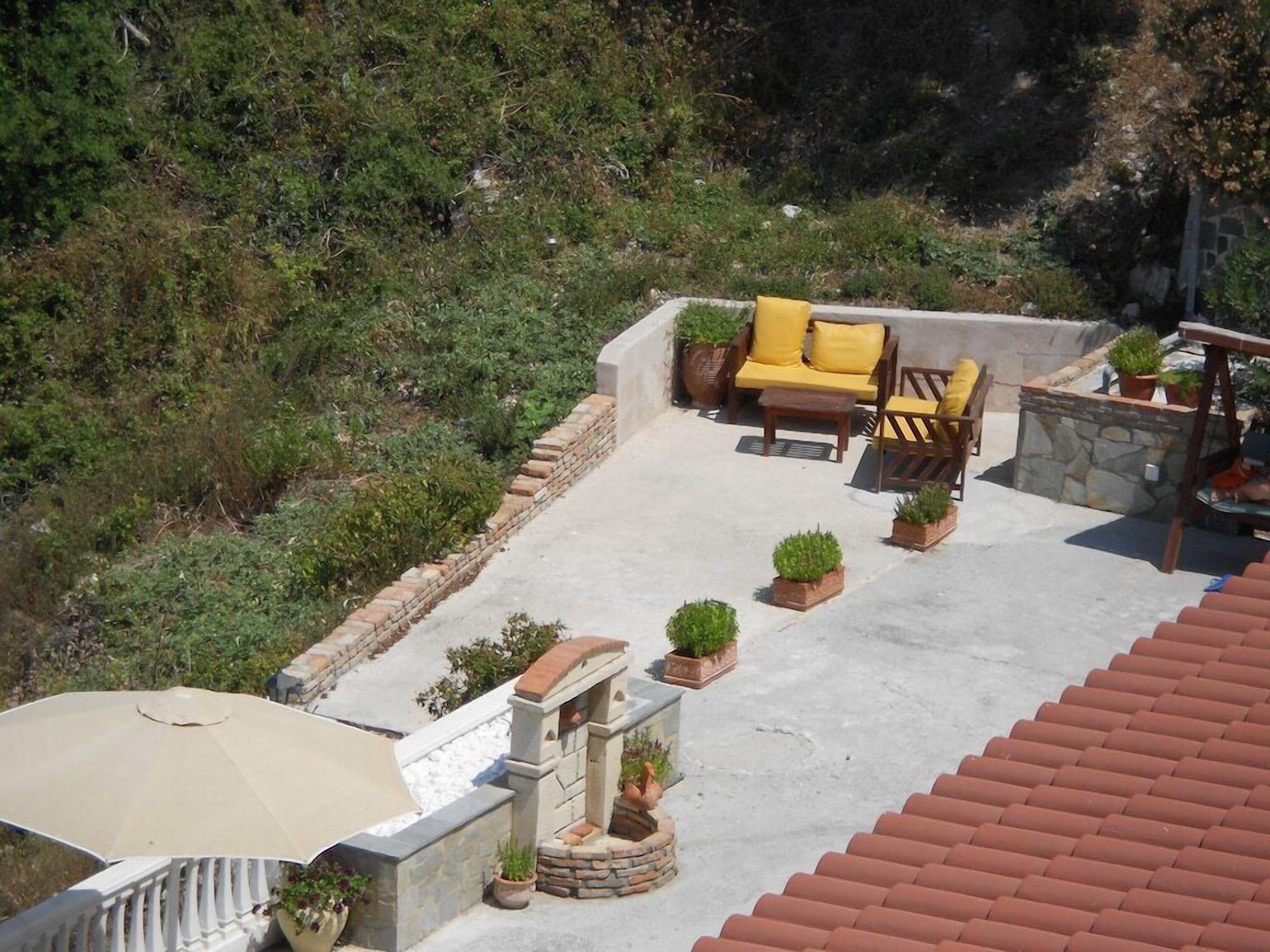 A rooftop terrace with outdoor furniture, potted plants, and a stone wall.