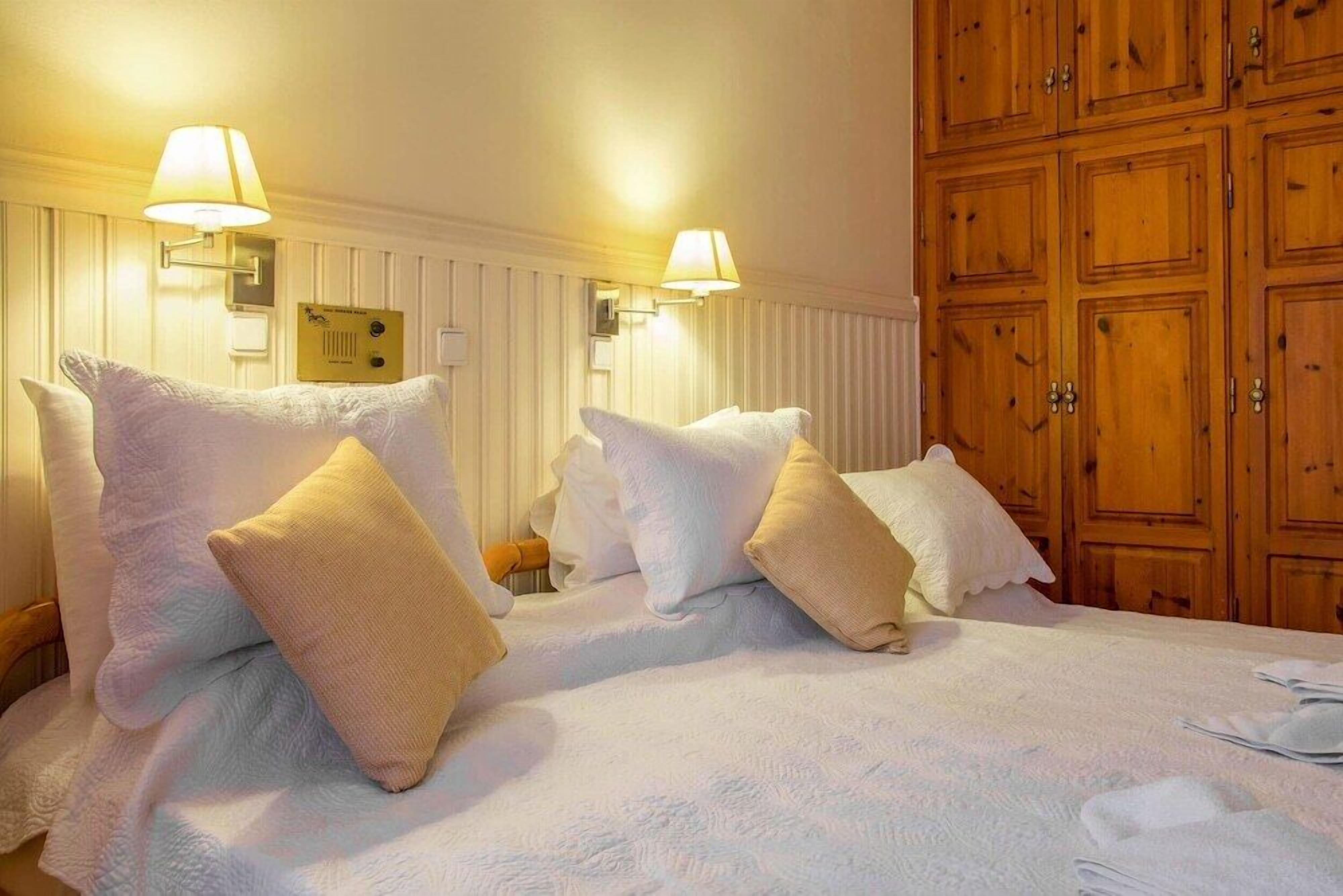 Een hotelkamer met een groot bed, meerdere kussens en houten kasten.