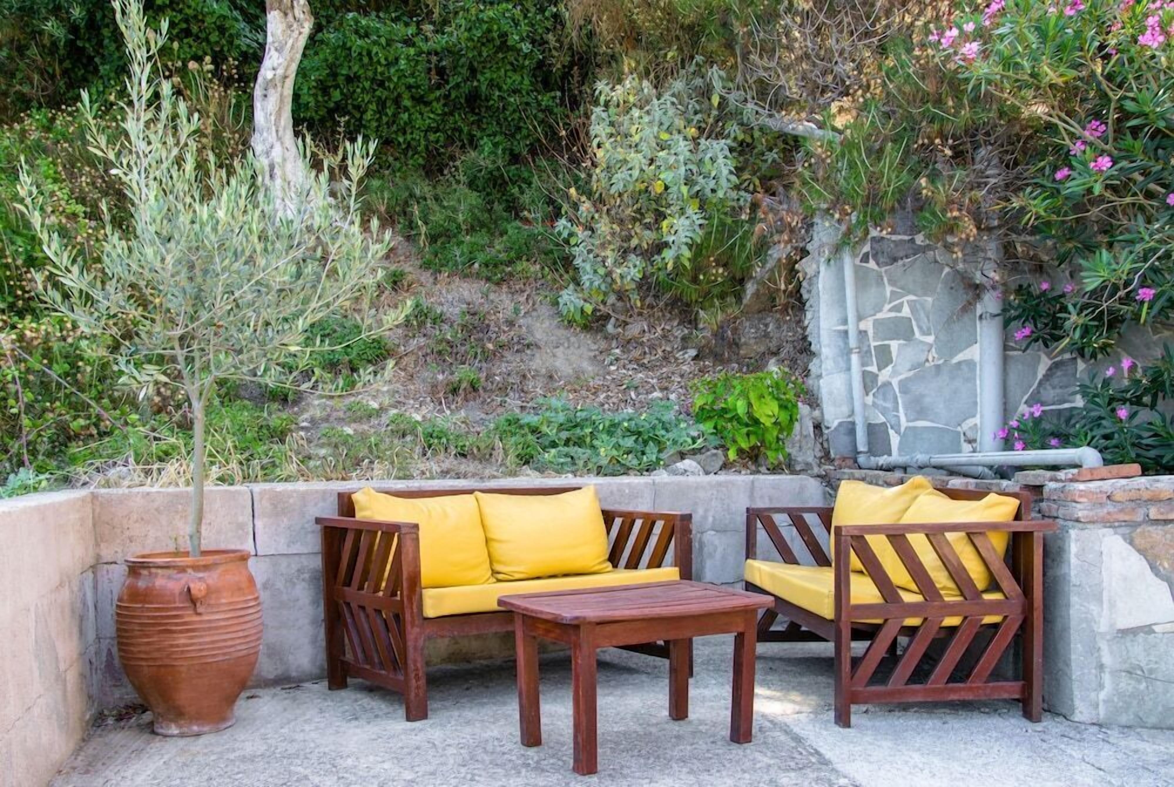 An outdoor seating area with a wooden sofa and chairs, a table, and a large terracotta pot.