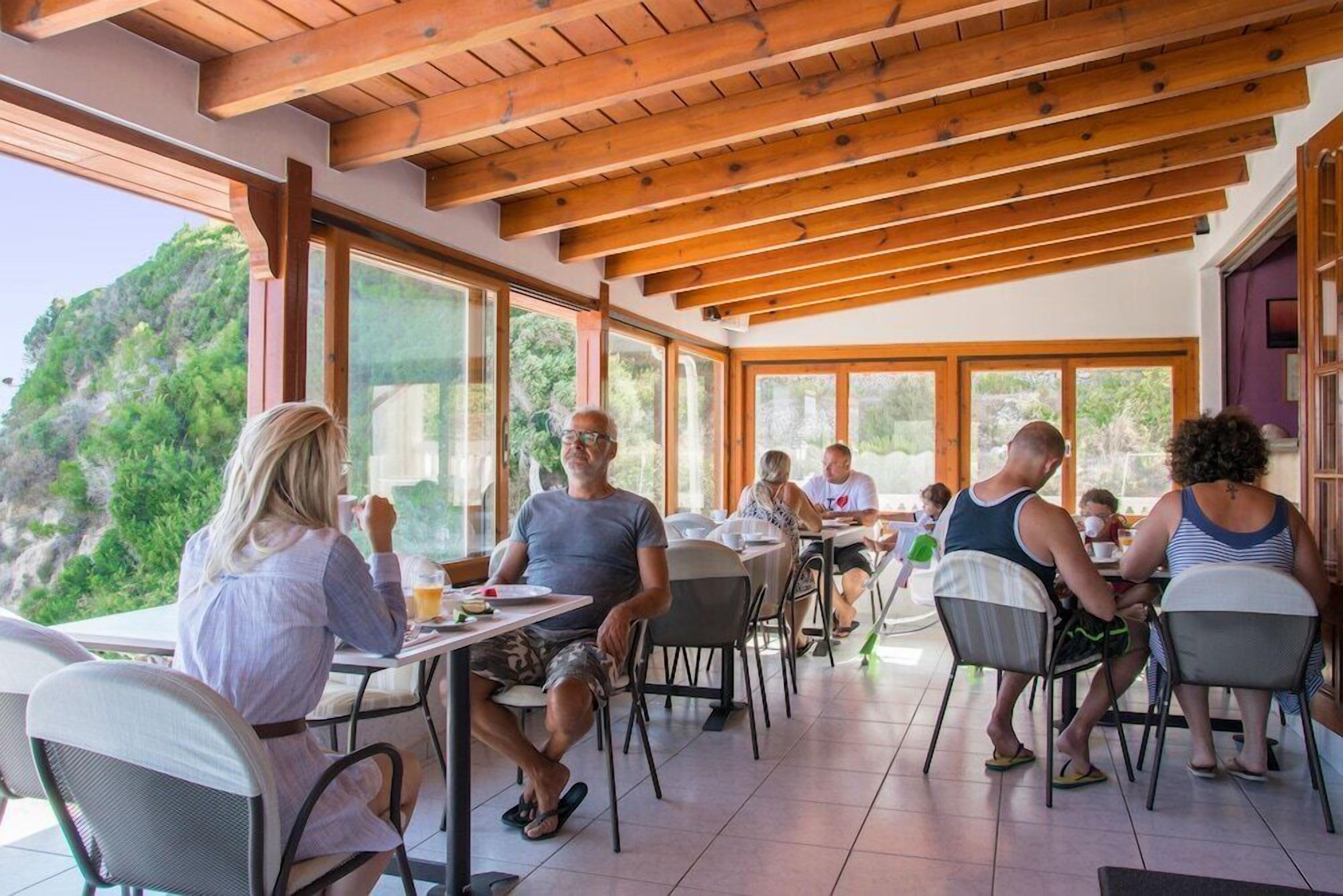 A restaurant with wooden beams, large windows, and a view of greenery.