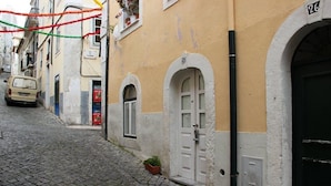 A narrow cobblestone street with a building featuring a white door and a small potted plant. - Portugal Ways Lisbon City Apartments (Lisbon)
