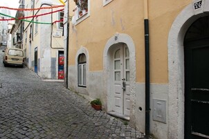 Una estrecha calle adoquinada con un edificio que tiene una puerta blanca y una pequeña planta en maceta.