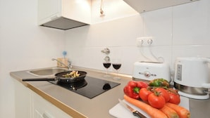 A modern kitchen with a stove, sink, and white cabinets. There are two wine glasses on the counter and a cutting board with vegetables. - Portugal Ways Lisbon City Apartments (Lisbon)